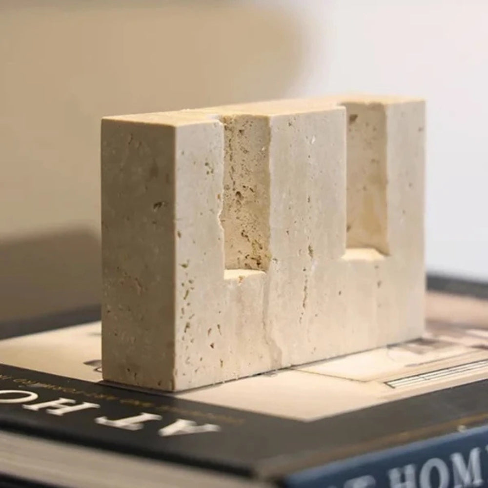 Beige travertine taper candle holder with two slots for candles, resting on a book.