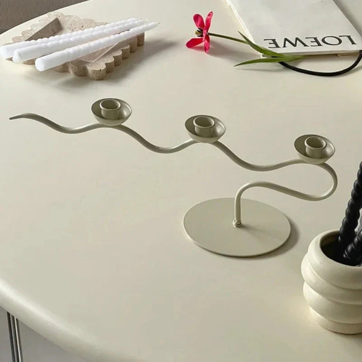 A cream-colored, three-headed twisted iron candle holder on a round base.