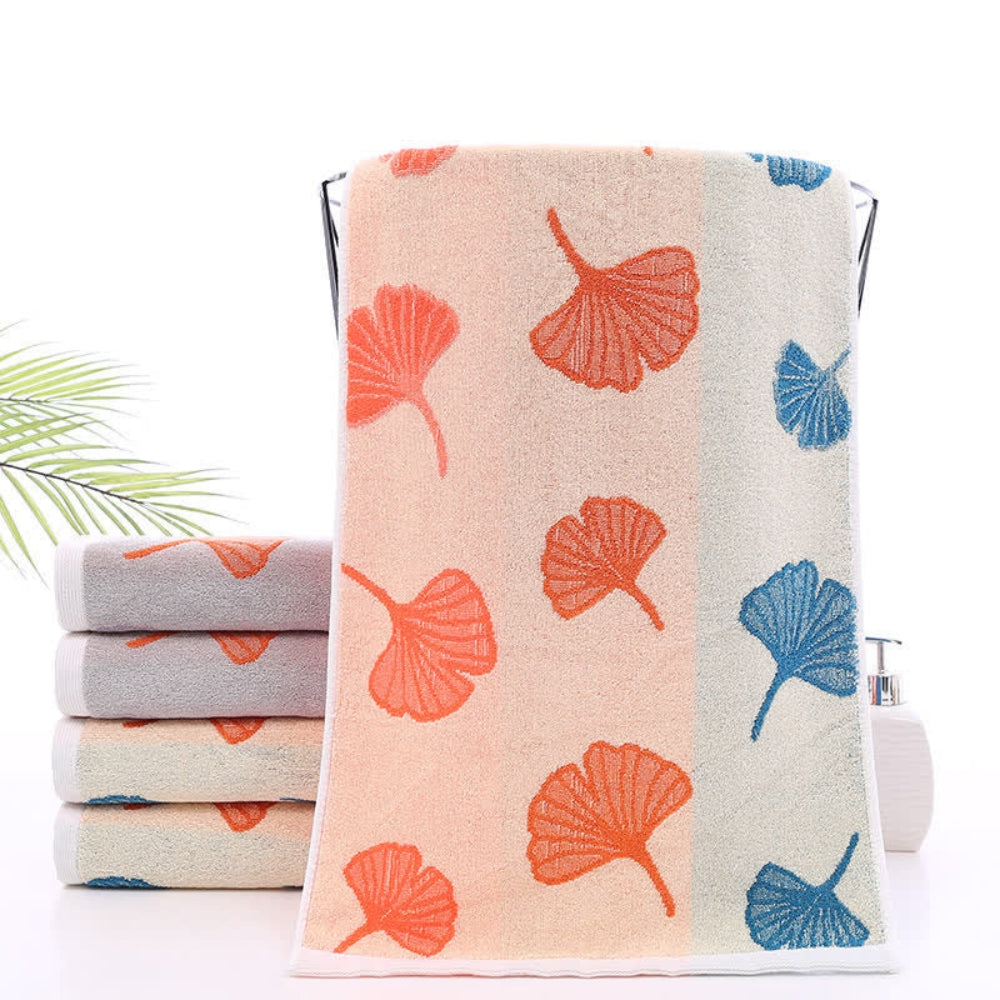 Stack of pure cotton bath towels with ginkgo leaf pattern in apricot, orange, gray, and blue.