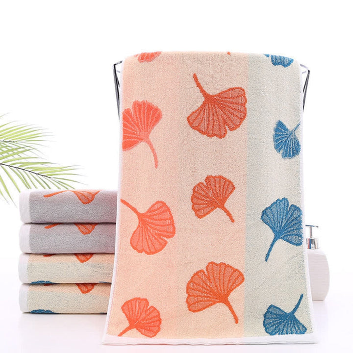 Stack of pure cotton bath towels with ginkgo leaf pattern in apricot, orange, gray, and blue.