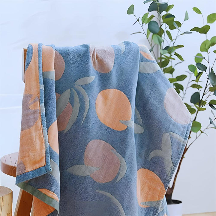 Blue cotton beach towel with an orange and pink fruit pattern, draped over a wooden stool.