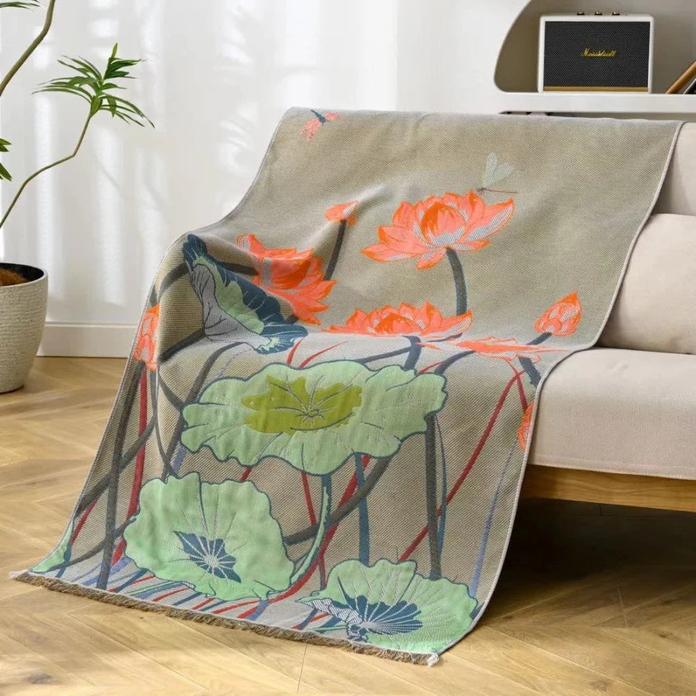 A beige cotton gauze bath towel with a vibrant lotus flower and leaf pattern draped over a sofa.