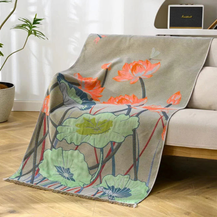 A beige cotton gauze bath towel with a vibrant lotus flower and leaf pattern draped over a sofa.