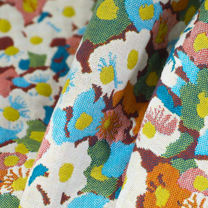 A close-up of a reversible cotton bath towel with a colorful floral pattern in blue, yellow, orange, and white.