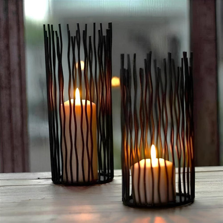 Two black iron desk candle holders with lit pillar candles inside, set on a wooden surface.
