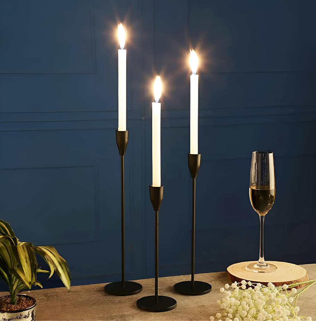 Three brushed metal taper candle holders of varying heights with white taper candles lit.