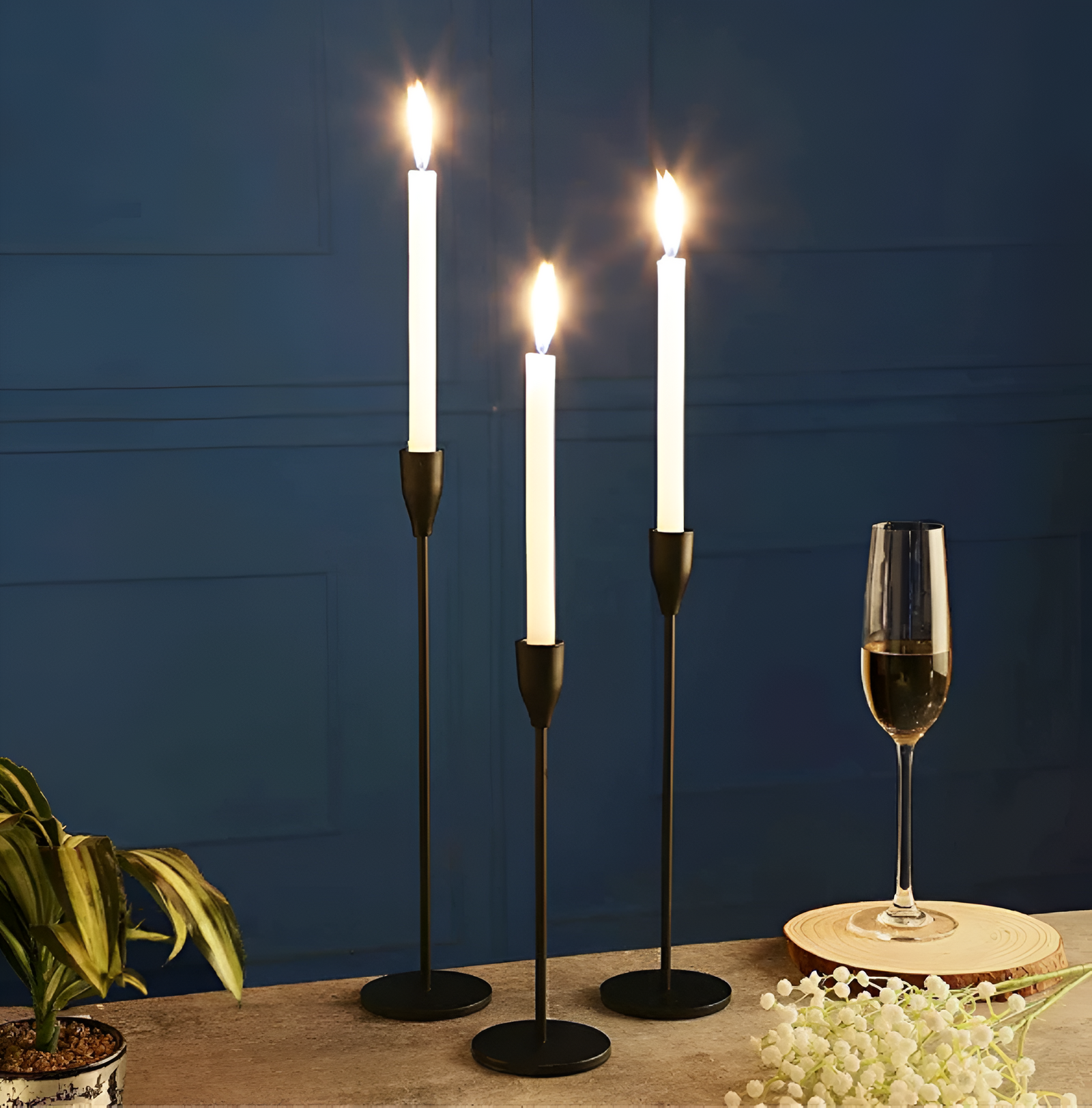 Three brushed metal taper candle holders of varying heights with white taper candles lit.