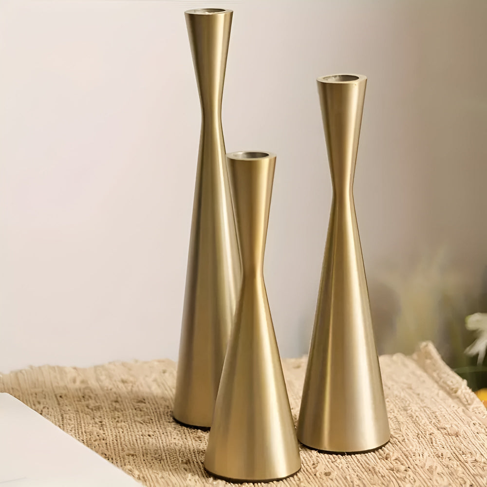 Three Nordic brass waist candlesticks of varying heights on a textured mat.