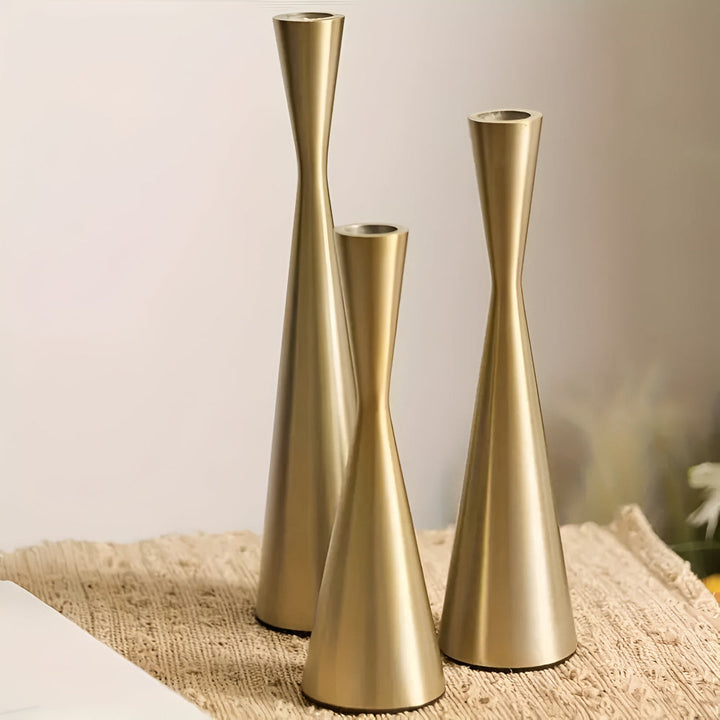Three Nordic brass waist candlesticks of varying heights on a textured mat.