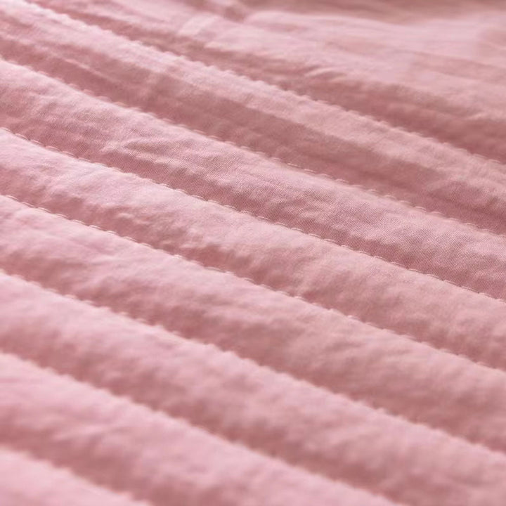 Close-up of a pink quilted cooling blanket with horizontal stitching.