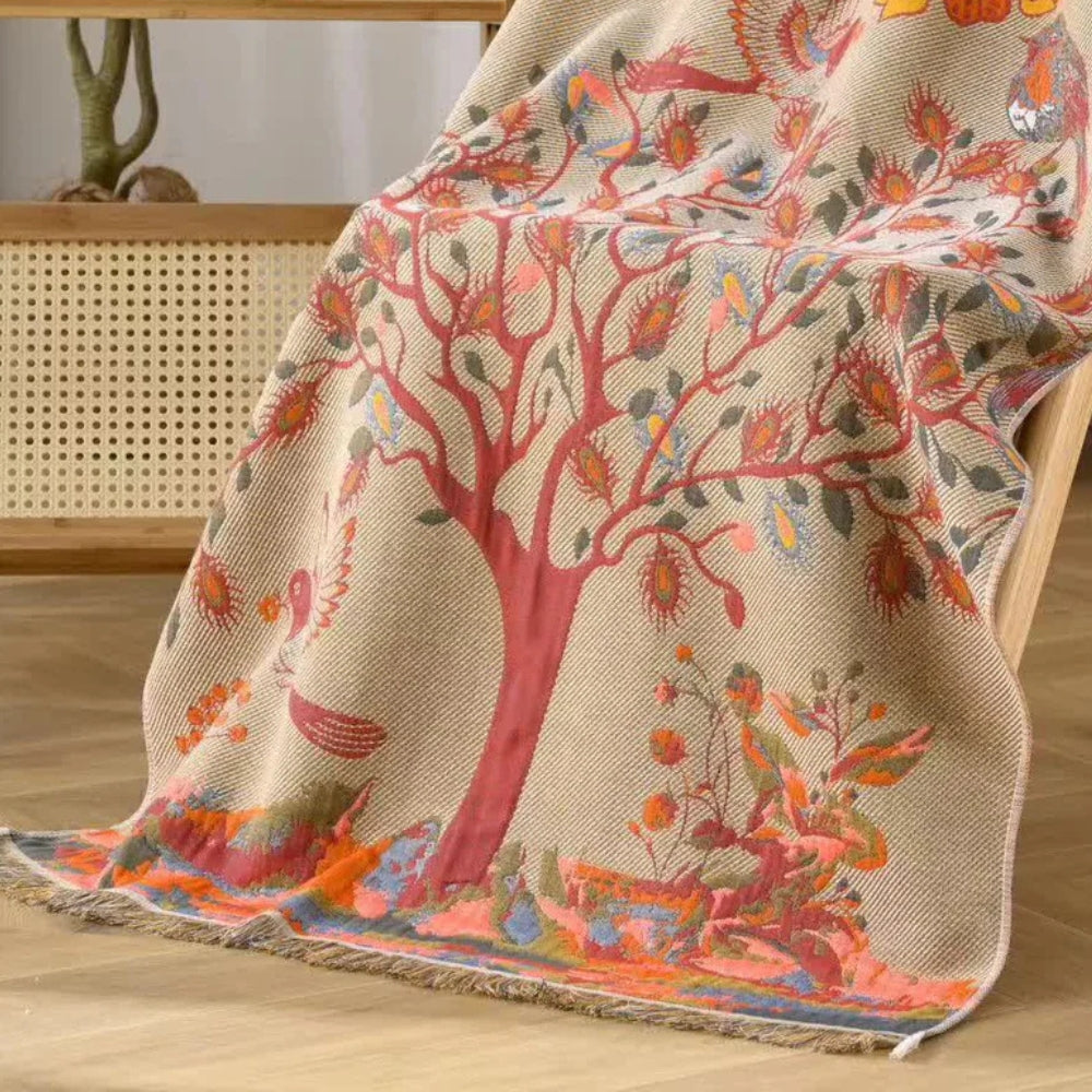 A beige cotton gauze throw blanket with a red tree design and colorful birds.