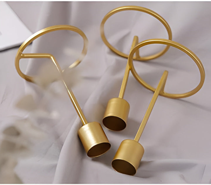 Three golden boho candle holders with circular tops and cylindrical bases on a draped fabric.