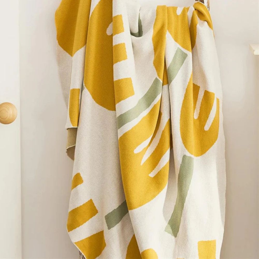 Knitted blanket with a yellow and green abstract floral pattern on a white background.