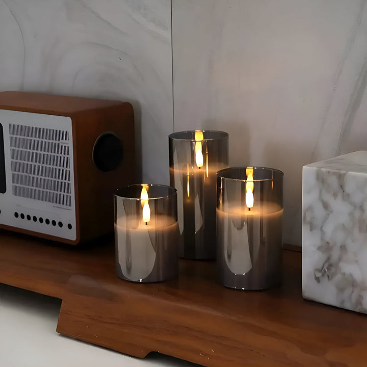 Three glass-encased flameless candles with realistic 3D LED flames on a wooden shelf.