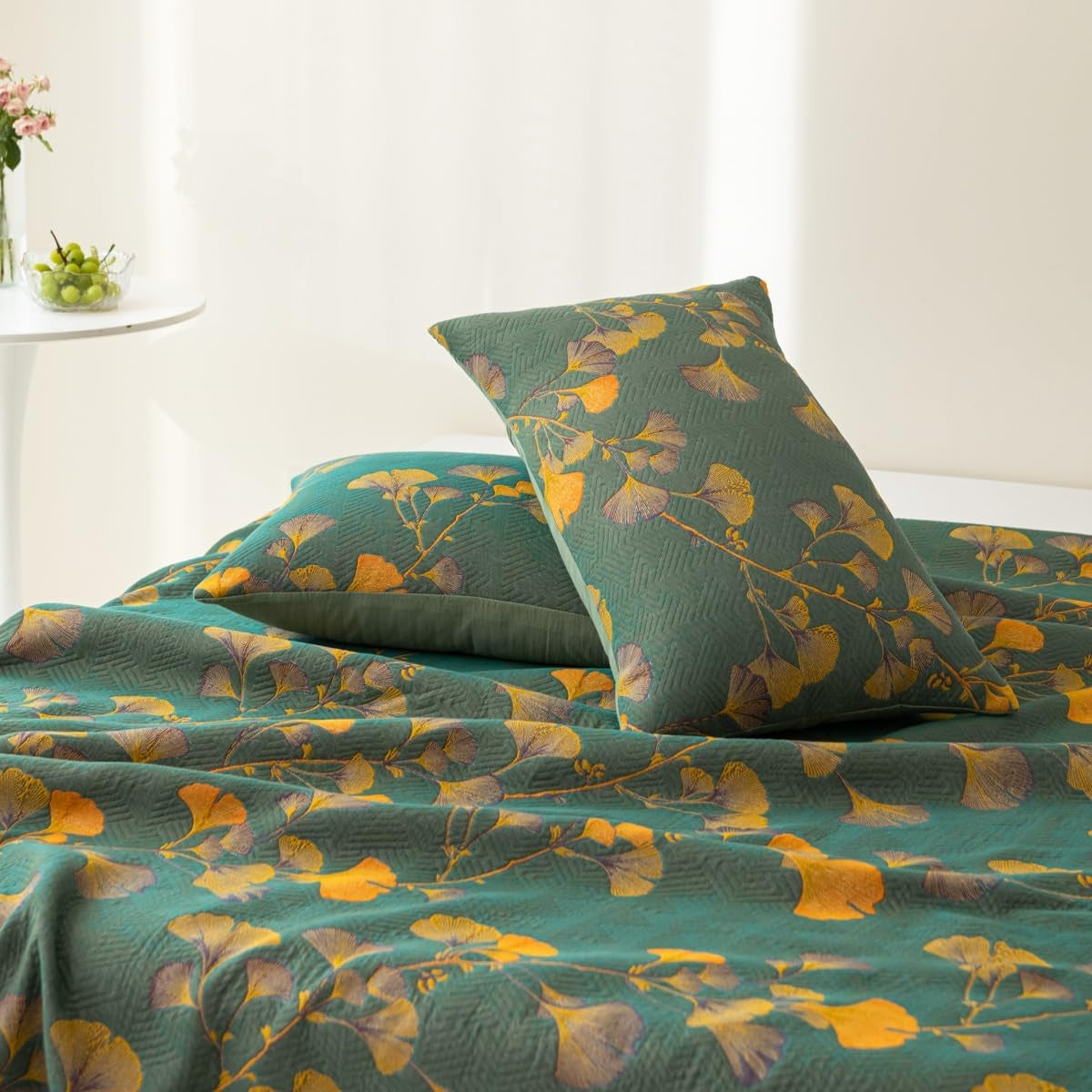 Green coverlet and pillows with a yellow and purple ginkgo leaf pattern.