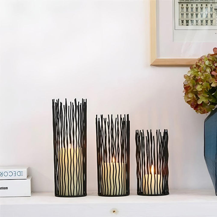 Three black iron candle holders with a geometric, wavy line design, in varying heights.