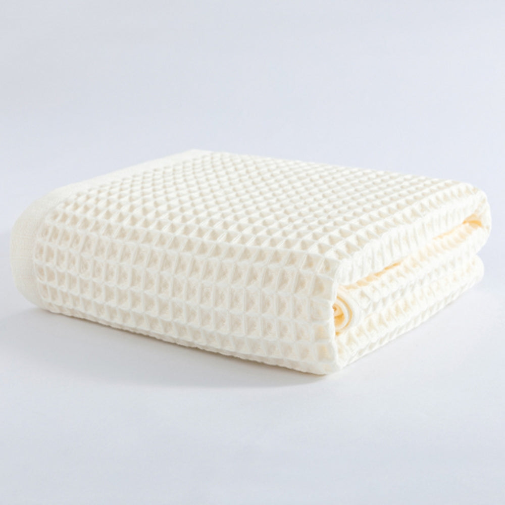 A folded cream-colored cotton waffle weave bath towel on a white background.