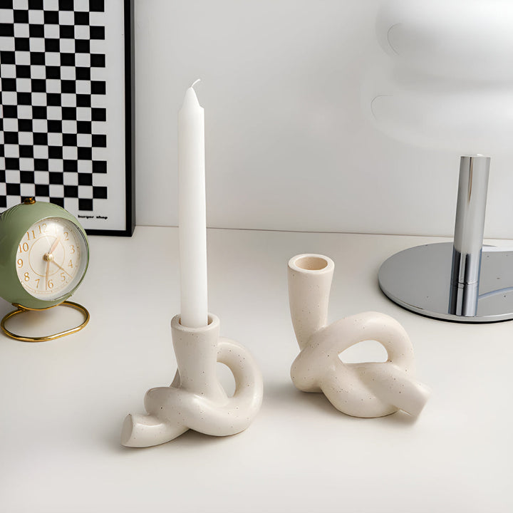 Two cream ceramic candle holders with a knotted design, one holding a white taper candle.