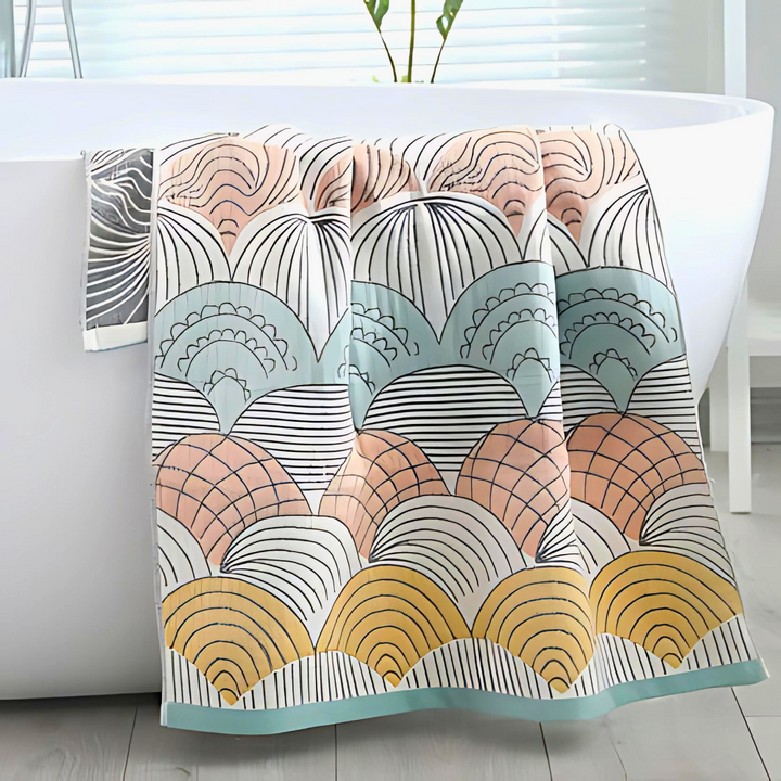 A cotton bath towel with a colorful shell-inspired jacquard weave draped over a white bathtub.