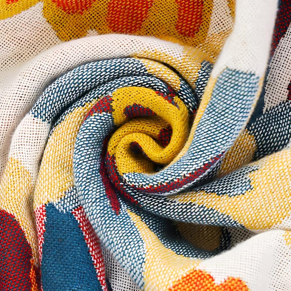Close-up of a rolled reversible cotton bath towel with a vibrant yellow, blue, and red floral pattern.