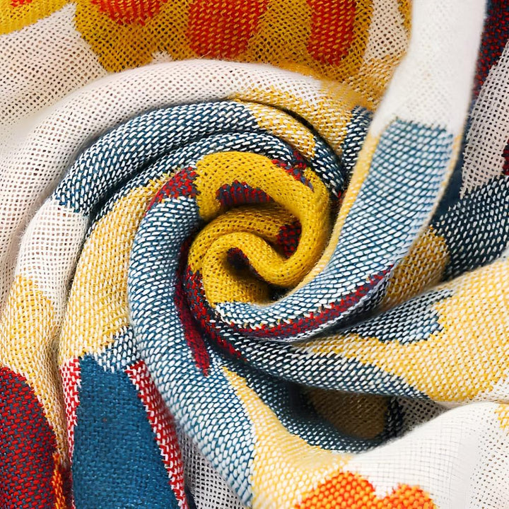Close-up of a rolled reversible cotton bath towel with a vibrant yellow, blue, and red floral pattern.