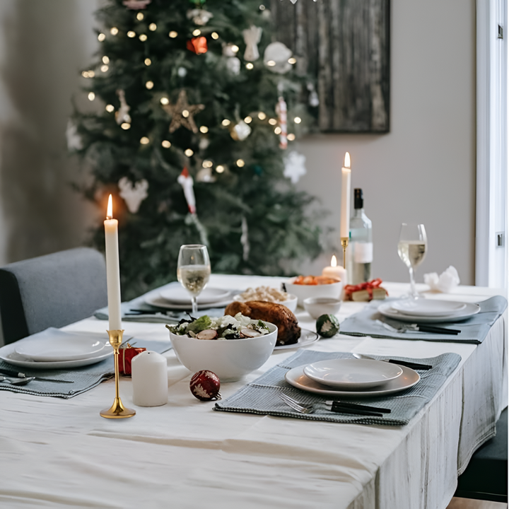 A gold taper candle holder with a lit candle on a table set for a holiday meal.