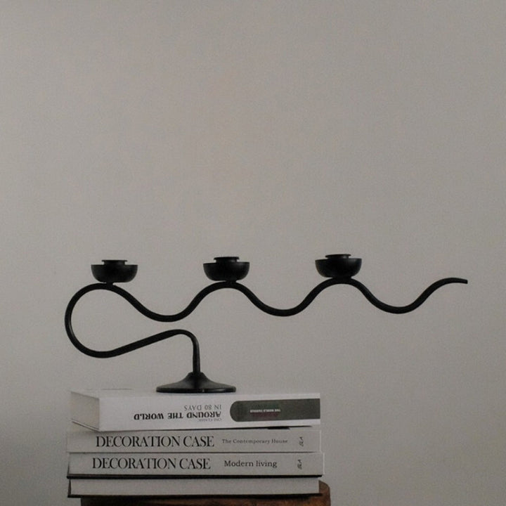 Black iron three-headed twisted candle holder with a wavy design, displayed on books.