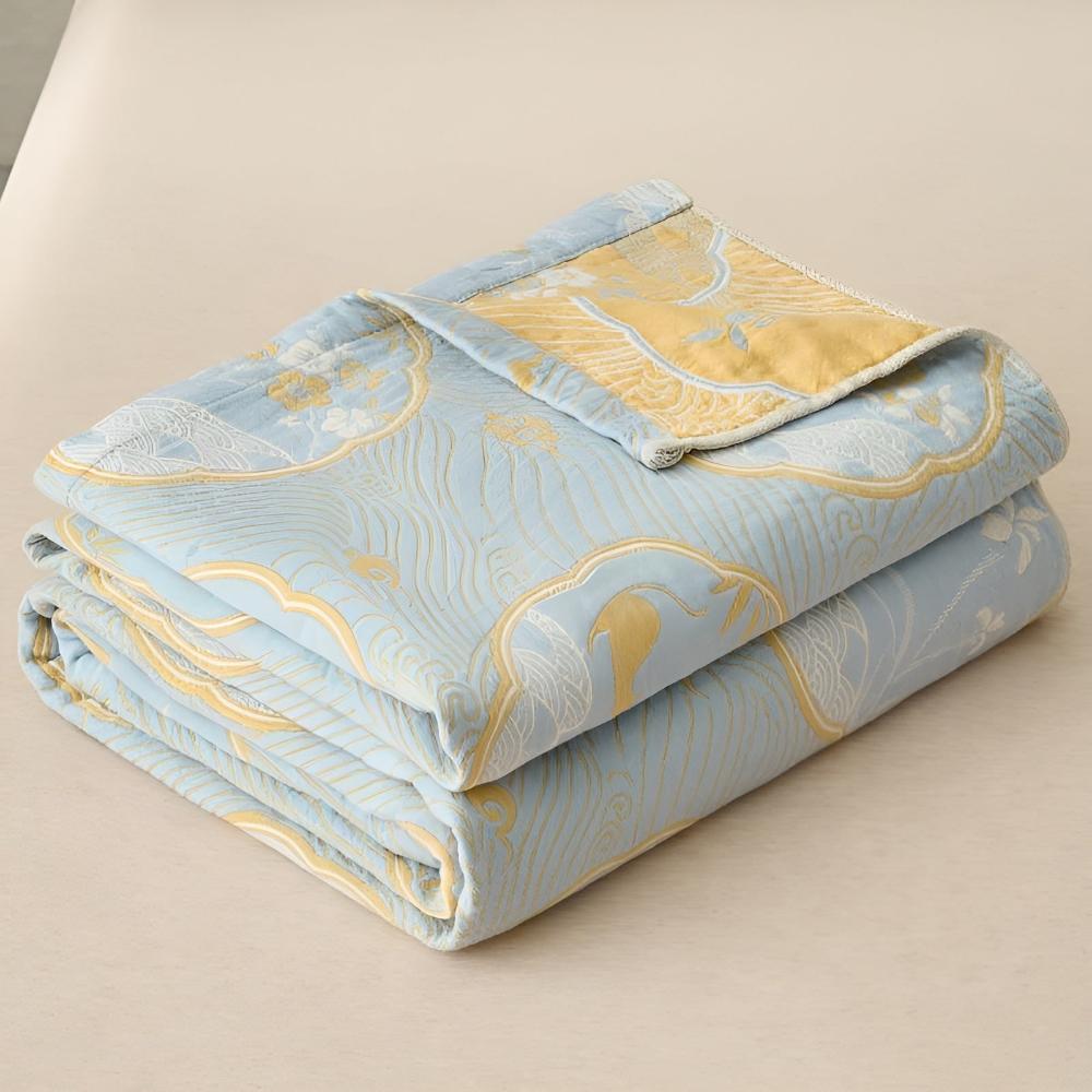 A folded light blue blanket with a reversible gold and blue pattern of waves and cranes.