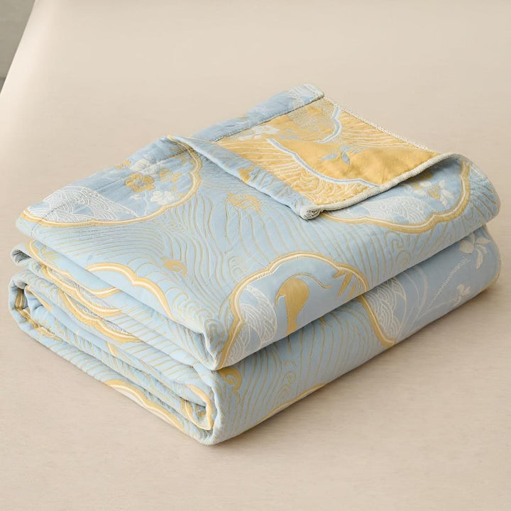 A folded light blue blanket with a reversible gold and blue pattern of waves and cranes.