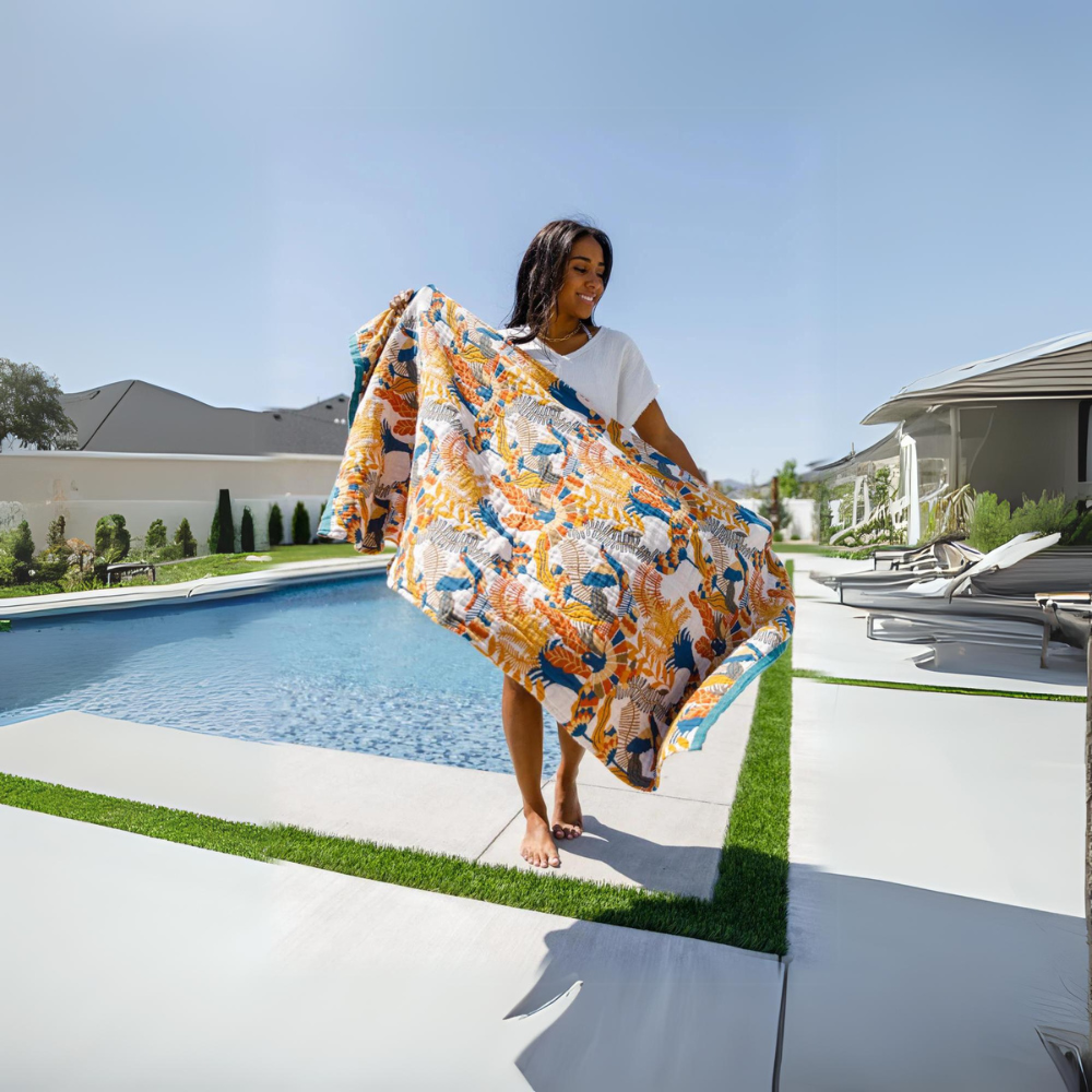 Woman holding a reversible cotton beach towel with a floral and bird print by a pool.