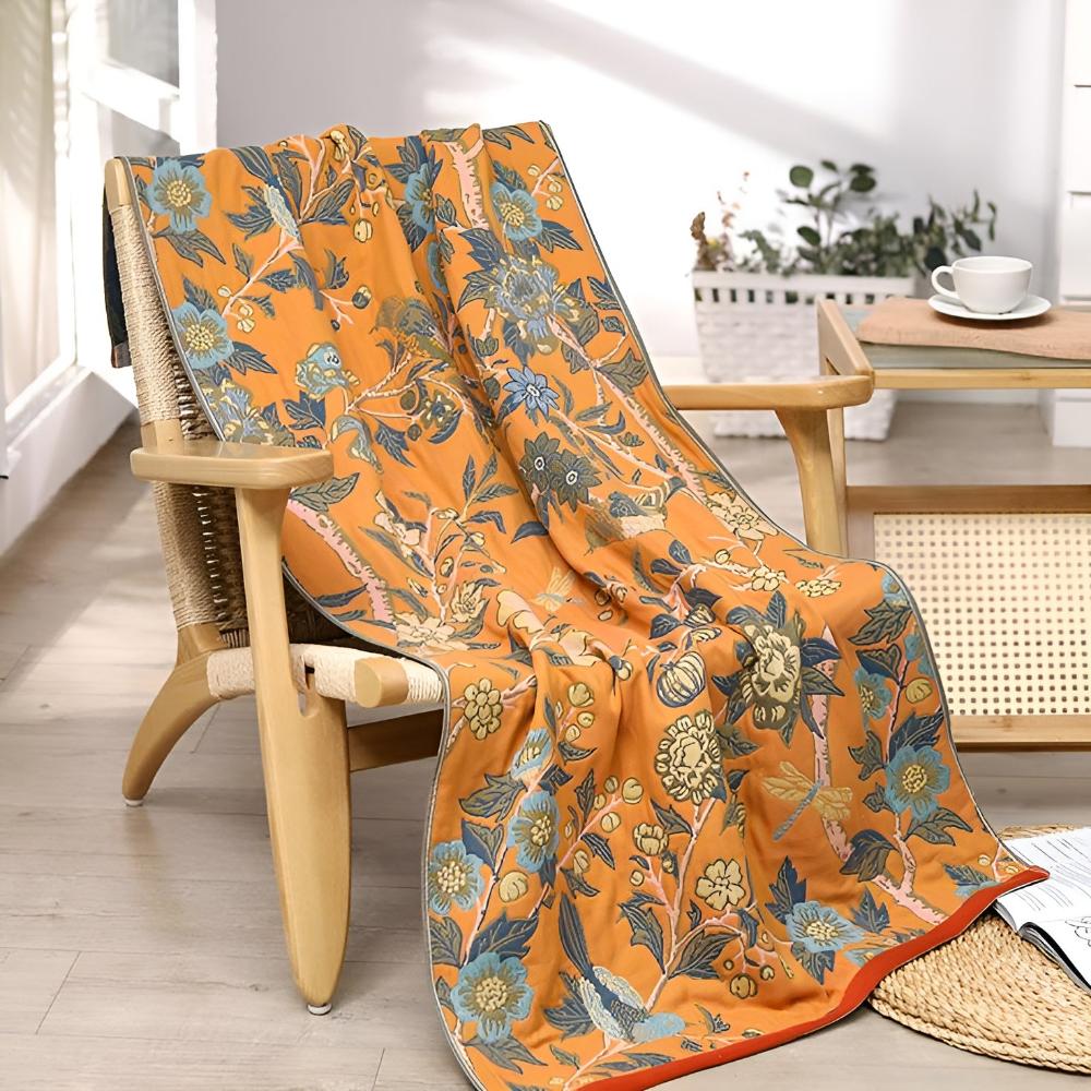 Orange cotton bath towel with a blue floral and bird pattern draped over a wooden chair.