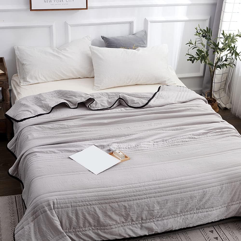 A light grey cooling blanket with a black trim is spread on a bed with white pillows.