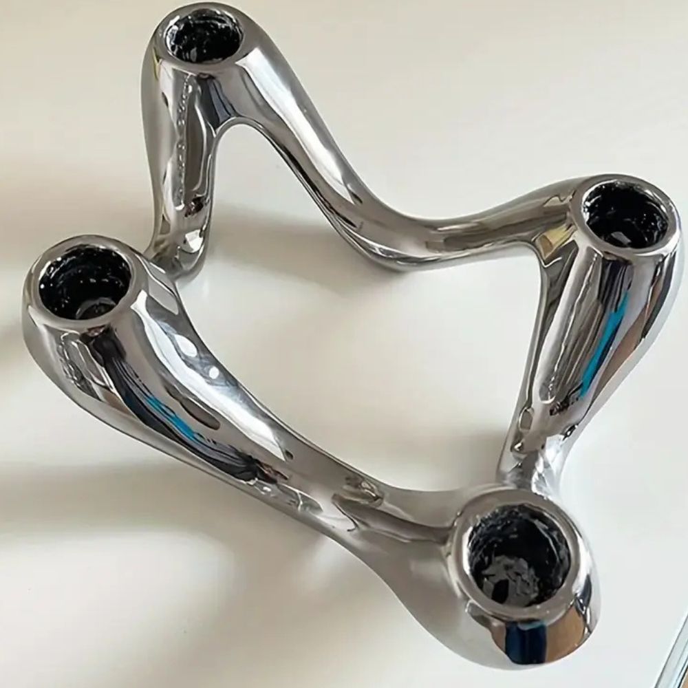 Silver ceramic candle holder with a flowing, ripple-inspired sculptural form and three openings for candles.