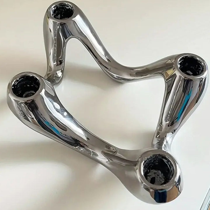 Silver ceramic candle holder with a flowing, ripple-inspired sculptural form and three openings for candles.