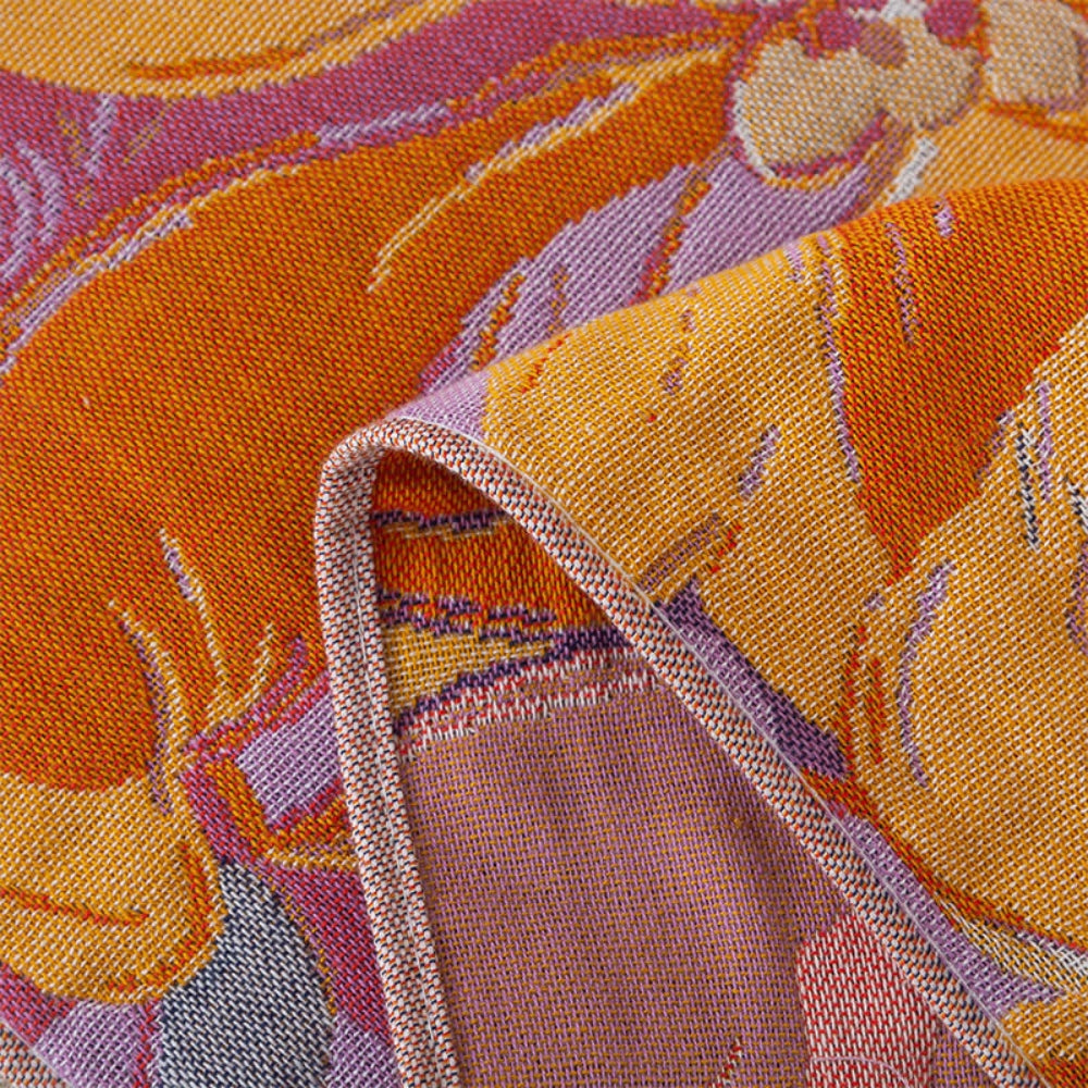 Close-up of a folded cotton gauze bath towel with a vibrant orange and purple floral pattern.