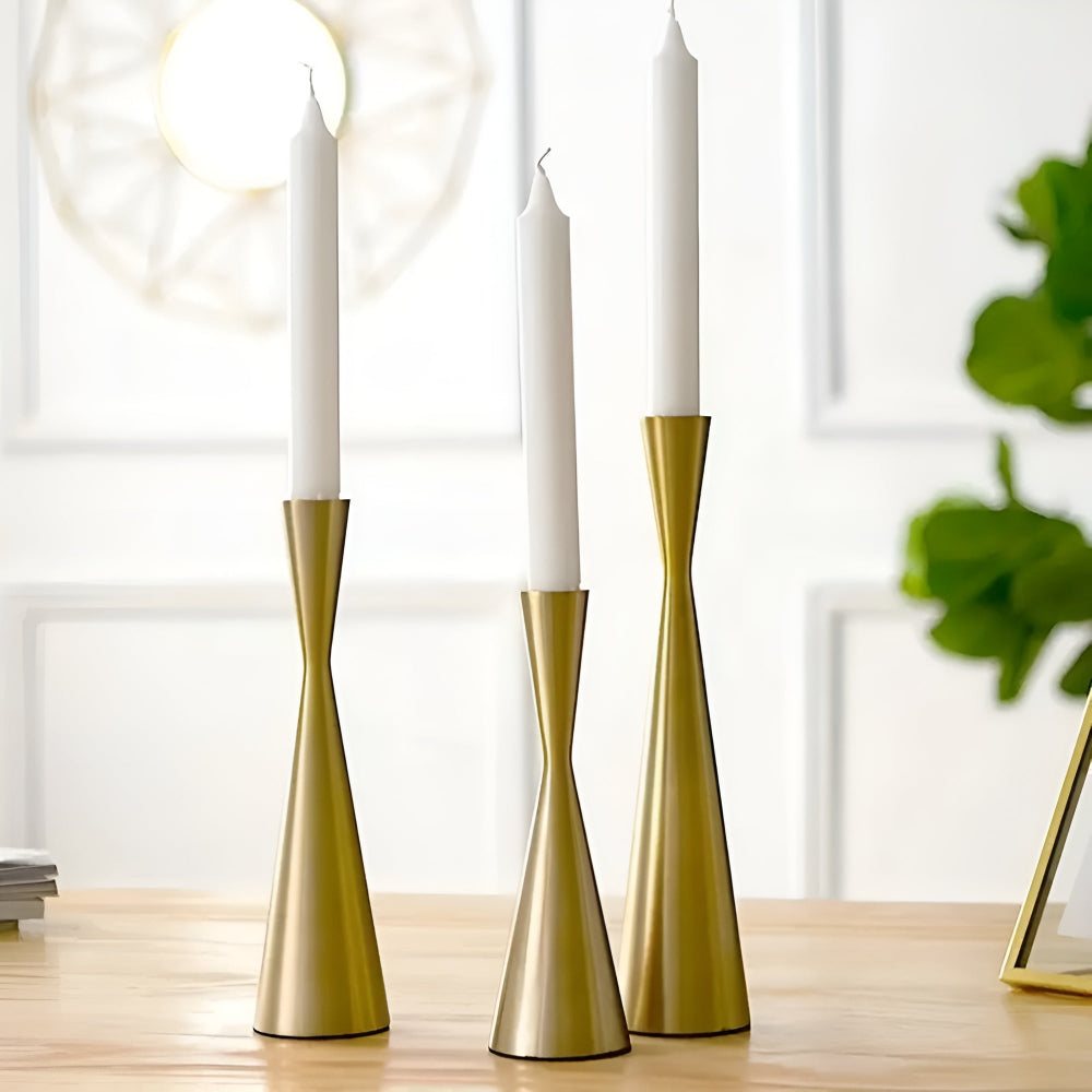 Three brass candlesticks with a waist design, each holding a white taper candle.