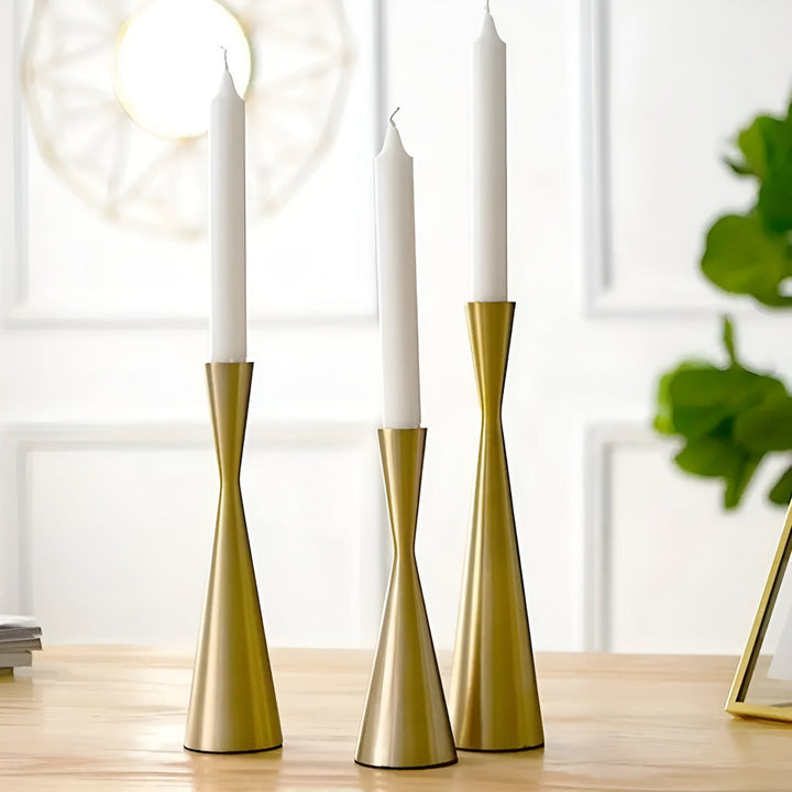 Three brass candlesticks with a waist design, each holding a white taper candle.