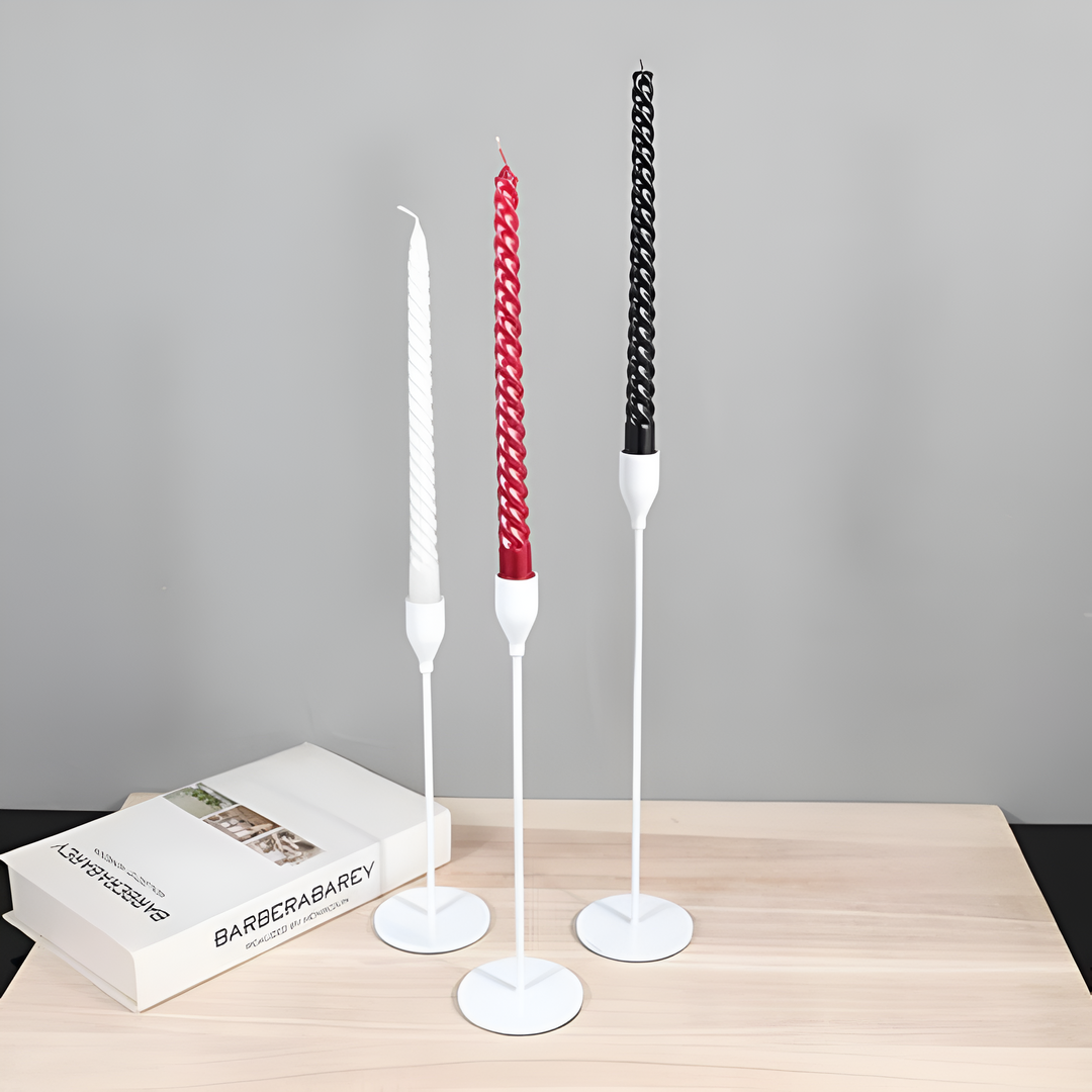 Three white taper candle holders of varying heights with white, red, and black candles.