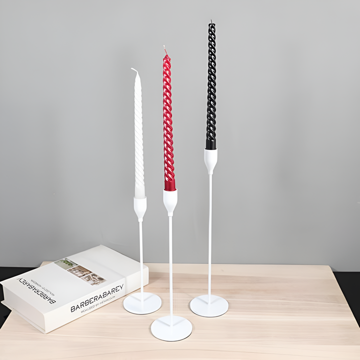Three white taper candle holders of varying heights with white, red, and black candles.