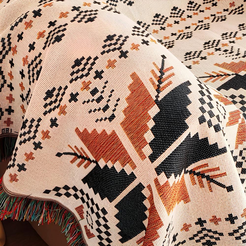A close-up of a Moroccan boho picnic mat with a geometric pattern in black, orange, and cream.