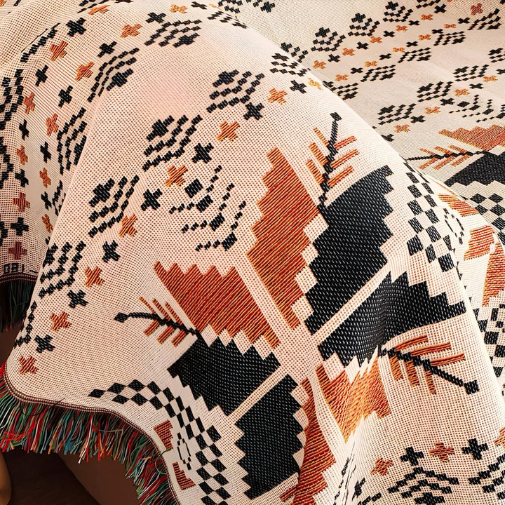 A close-up of a Moroccan boho picnic mat with a geometric pattern in black, orange, and cream.