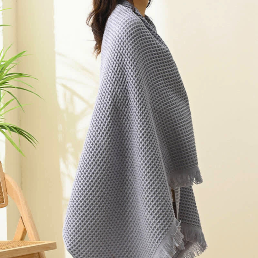 Gray cotton waffle weave bath towel draped over a person, showing fringe detail.