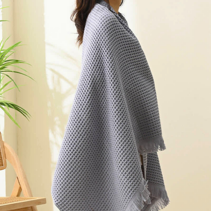 Gray cotton waffle weave bath towel draped over a person, showing fringe detail.