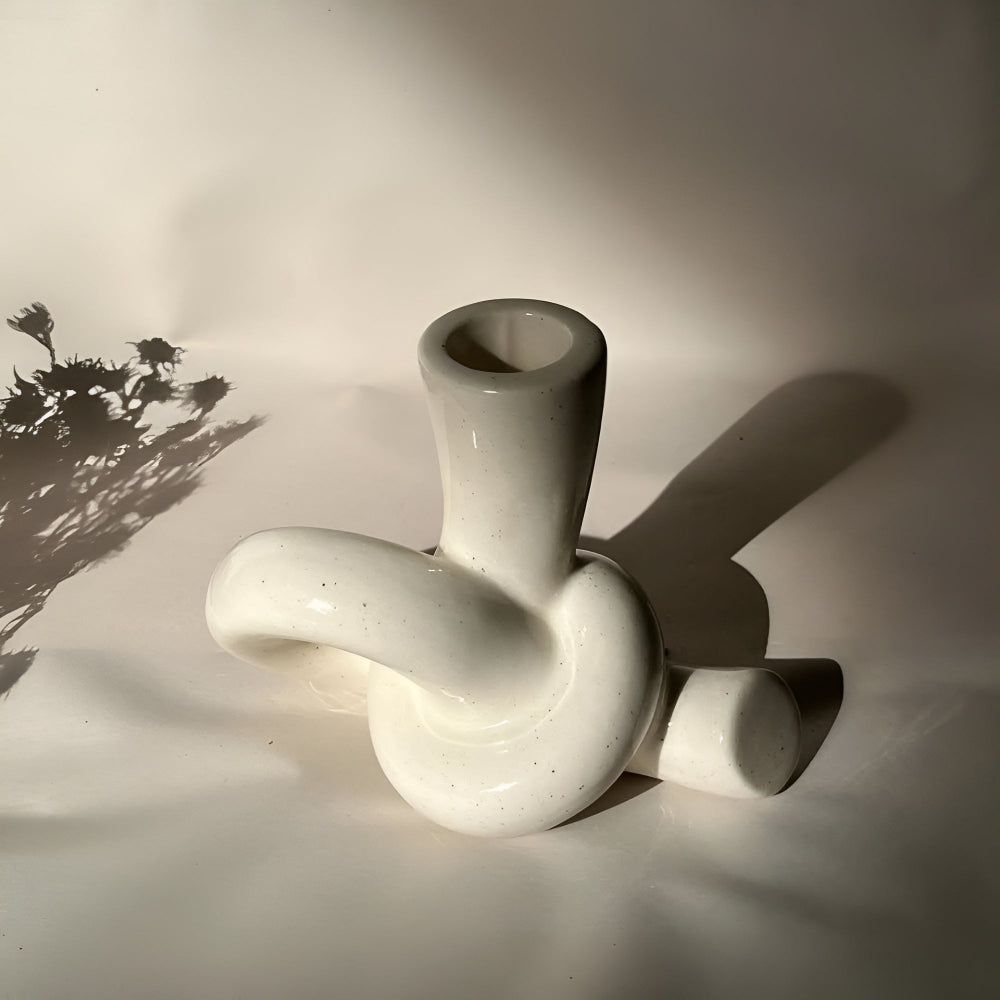 White ceramic candle holder with a knotted design, casting a shadow on a white surface.