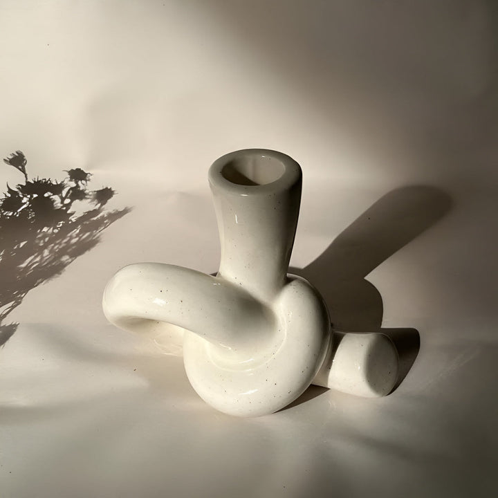 White ceramic candle holder with a knotted design, casting a shadow on a white surface.
