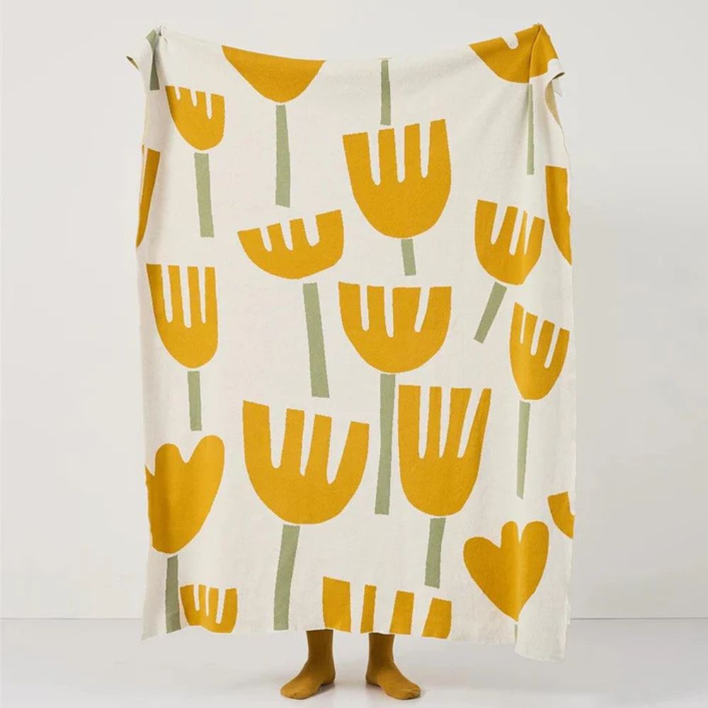 Cream knitted blanket with a repeating pattern of yellow tulips and green stems.