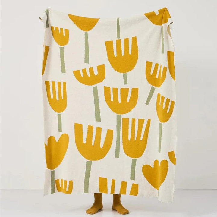 Cream knitted blanket with a repeating pattern of yellow tulips and green stems.