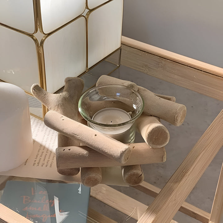 Driftwood tealight holder with a glass insert and a lit candle, surrounded by wooden pieces.