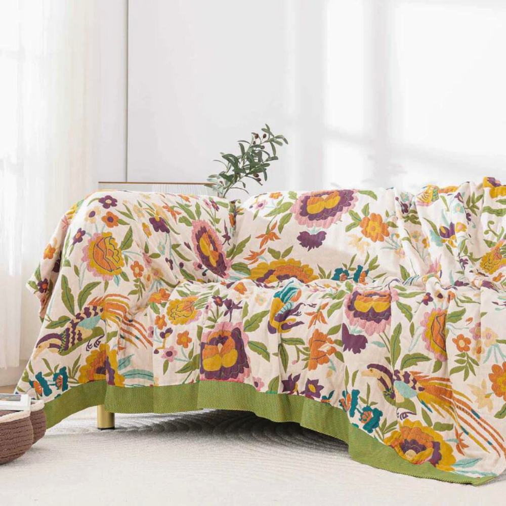 A sofa draped with a coverlet featuring a vibrant floral and bird pattern in shades of yellow, orange, purple, and green.