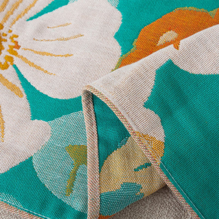 Close-up of a cotton gauze bath towel with a tropical floral pattern in teal, orange, and white.